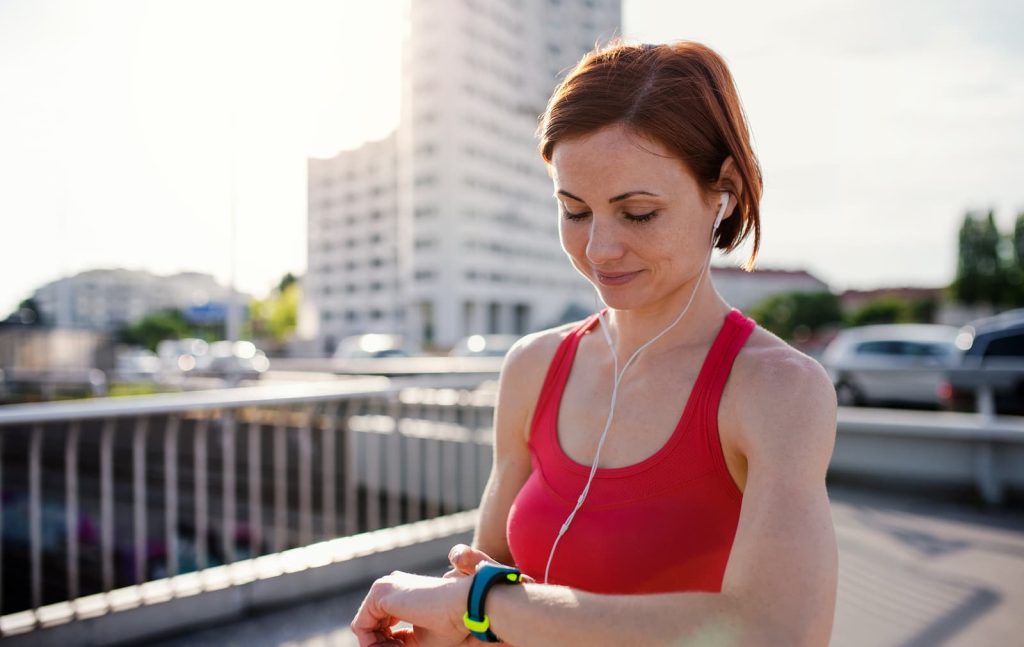 Young woman runner with earphones in city, using smartwatch.