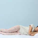 Woman in pyjamas sleeping on bed with blue background