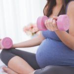 Pregnant woman doing exercise on her bed using dumbbell
